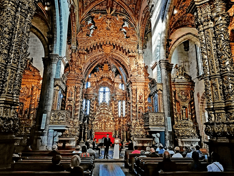 An audience watching a performance inside the ornate Sao Francisco Church in Porto, surrounded by the church's intricate Baroque architecture. 