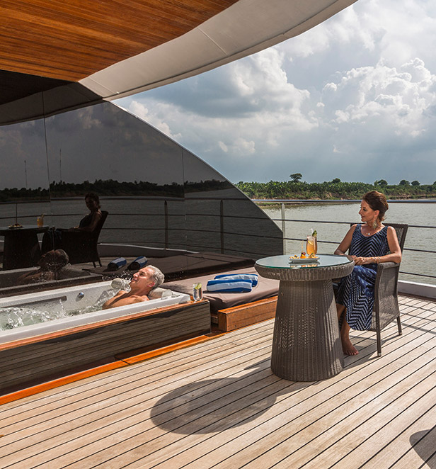 A man and woman relaxing on the outdoor terrace of the Royal Panorama Suite with the Mekong river in the background, Scenic Spirit  