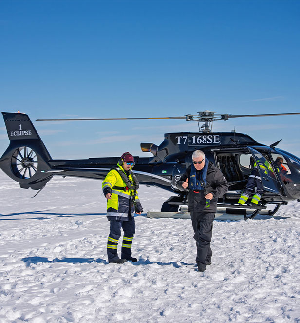 black helicopter landing on snow with 2 people 